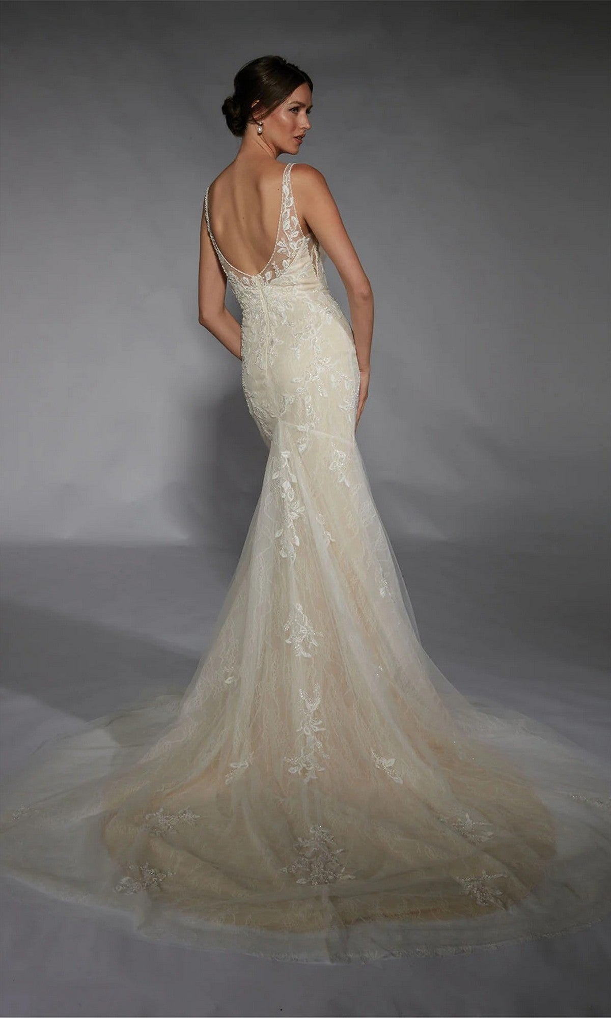A woman models the Long White Dress: Alyce 7119, an ivory mermaid bridal gown with exquisite lace, a low back, and a long train, set against a gray studio backdrop.